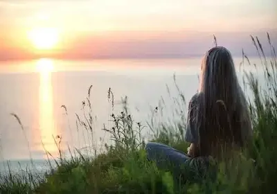 Frau sitzt entspannt im Gras und blickt auf einen großen See