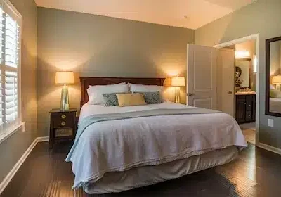 Blick in ein Schlafzimmer, das Bett ist ordentlich gemacht, mehrere Kissen, die Nachttischlampen sind angeschalten